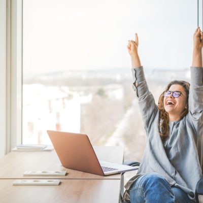 A happy and cheerful businesswoman raising fists with ambition. Personal success and career ladder. Business achievement and promotion concept